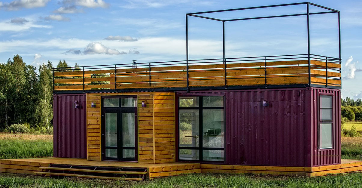 Une maison container partiellement recouverte d’un bardage en bois et surmontée d’un toit terrasse. 