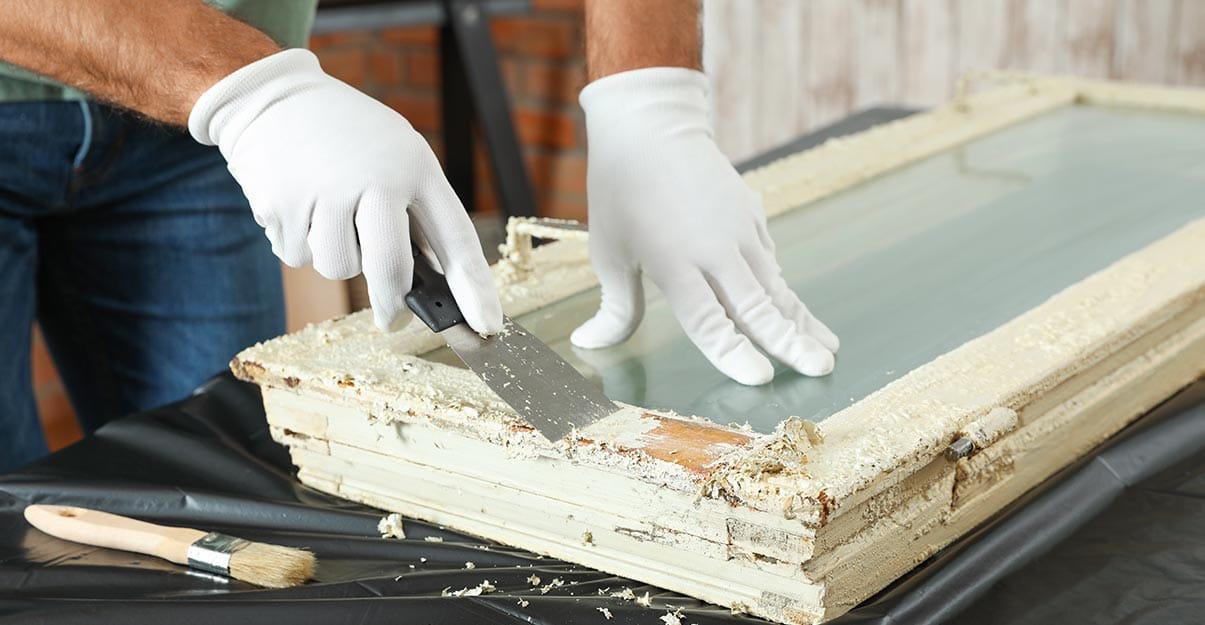 Gratter l’ancienne peinture d’une fenêtre en bois avec un petit couteau à enduire