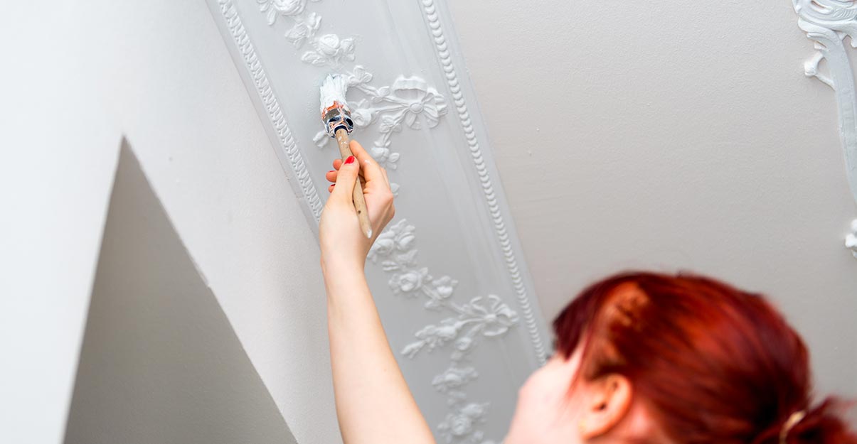 Une femme peint un plafond avec des moulures